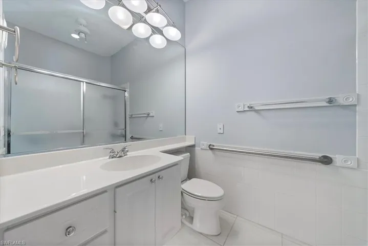 Full bath with tile patterned flooring, vanity, tile walls, toilet, and an enclosed shower