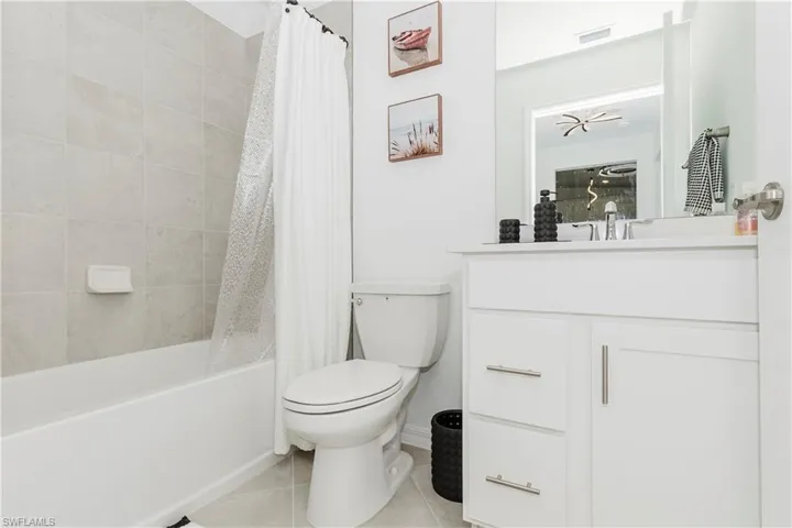 Bathroom with tile patterned floors, toilet, vanity, shower / tub combo with curtain, and baseboards