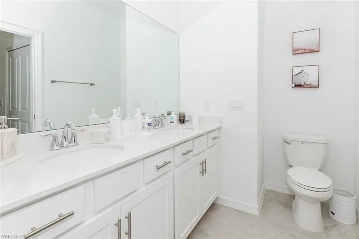 Full bath with double vanity, toilet, and baseboards