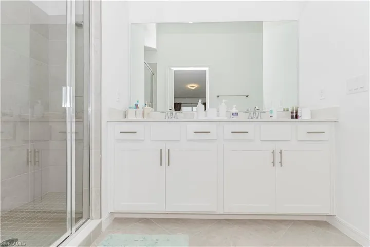 Bathroom featuring a shower stall, double vanity, and baseboards