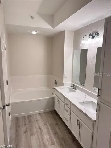 Full bathroom with double vanity, a bath, and light wood-style floors