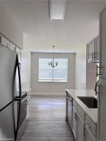 Kitchen with appliances with stainless steel finishes, light wood-type flooring, pendant lighting, a textured ceiling, and light stone countertops