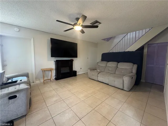 Living room featuring a fireplace, a textured ceiling, stairway, light tile patterned flooring, and ceiling fan