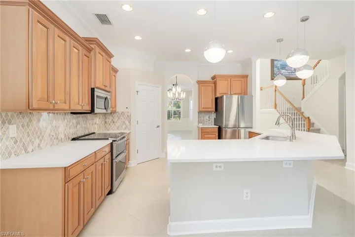 Kitchen with backsplash, hanging light fixtures, appliances with stainless steel finishes, crown molding, and a chandelier