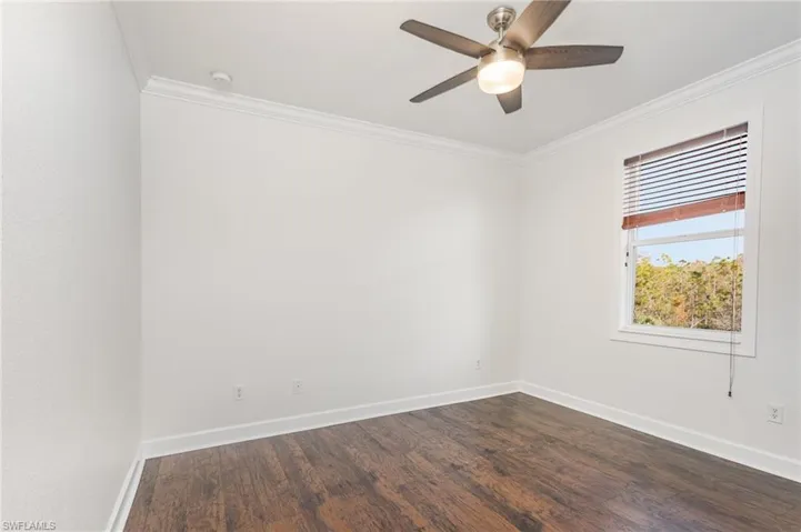 Empty room with ornamental molding, dark wood-style floors, and ceiling fan
