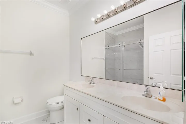 Full bath featuring crown molding, double vanity, and a marble finish shower