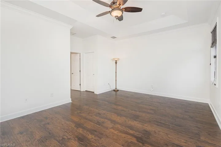 Empty room featuring a tray ceiling, crown molding, dark wood finished floors, and a ceiling fan