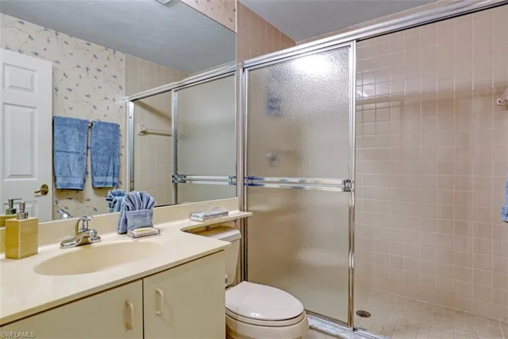 Bathroom with wallpapered walls, a stall shower, and vanity