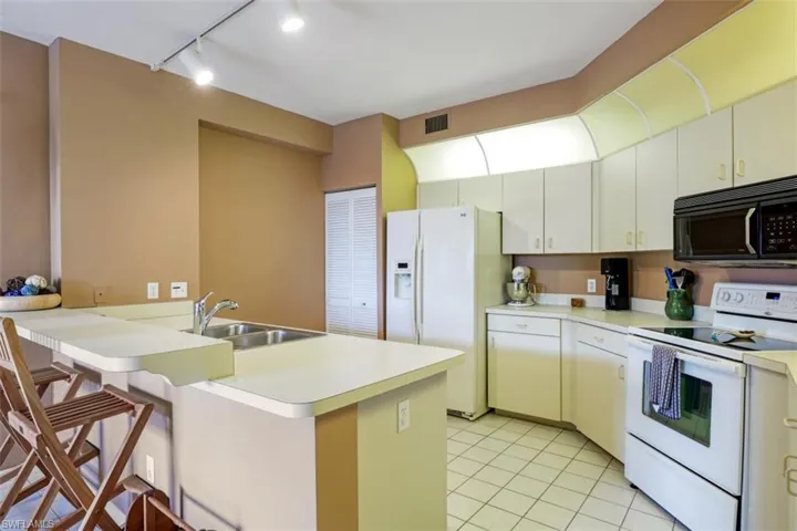 Kitchen featuring white appliances, light tile patterned floors, rail lighting, light countertops, and a peninsula