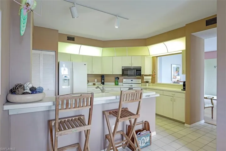 Kitchen with white appliances, light countertops, a kitchen breakfast bar, light tile patterned floors, and rail lighting