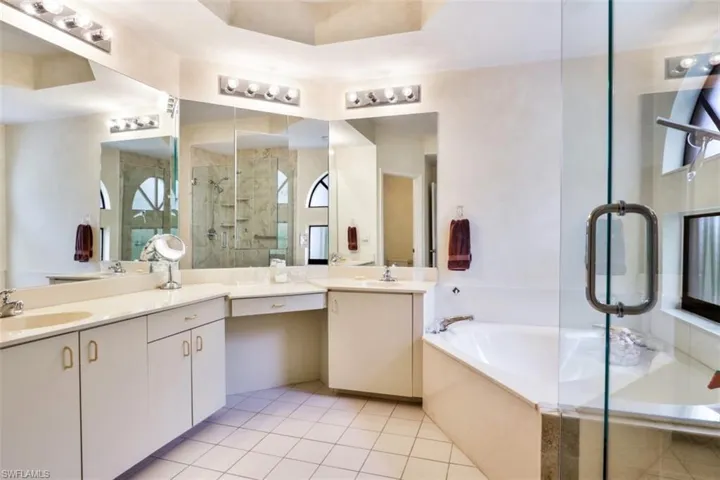 Full bath with two vanities, a shower stall, a garden tub, tile patterned floors, and plenty of natural light