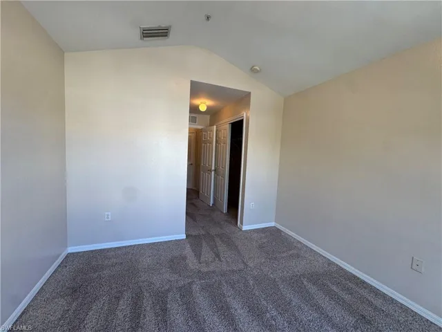 Spare room featuring dark carpet and lofted ceiling