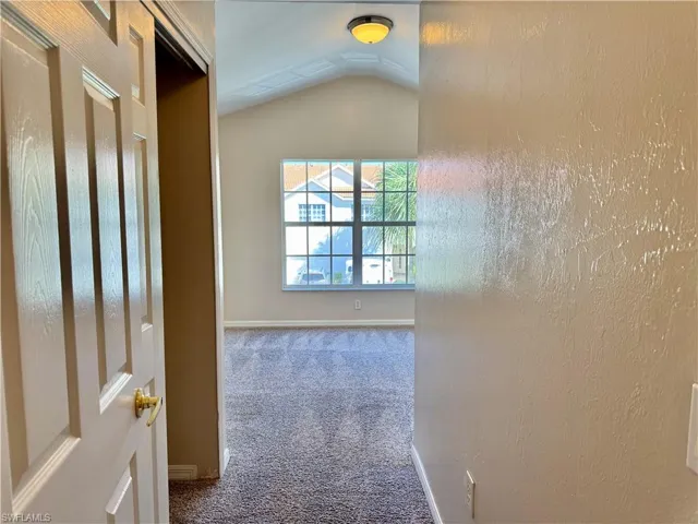 Hall with carpet flooring, vaulted ceiling, and a textured wall