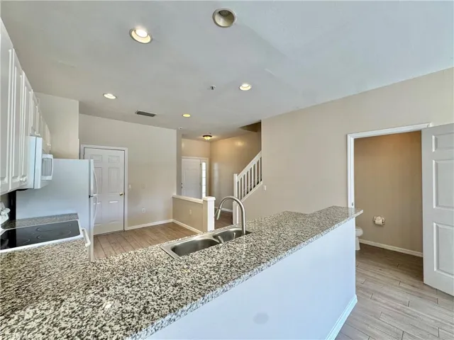 Kitchen featuring light wood finished floors, a peninsula, electric range, light stone countertops, and white cabinetry