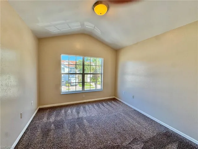 Carpeted spare room featuring vaulted ceiling and baseboards