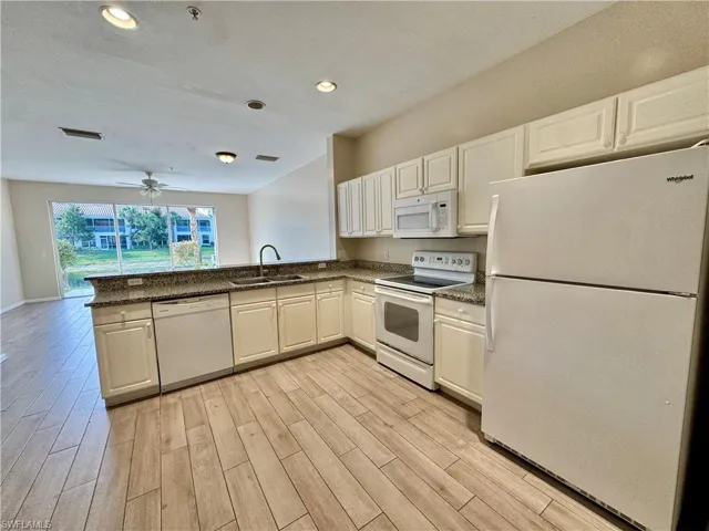 Kitchen with white appliances, recessed lighting, white cabinetry, light wood-type flooring, and dark stone counters