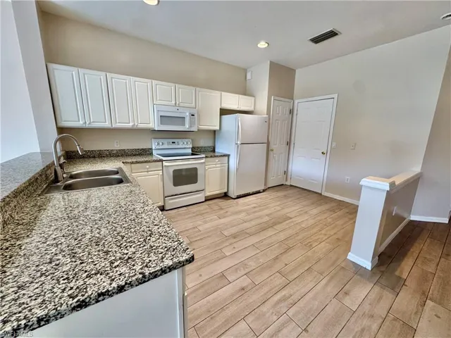 Kitchen featuring dark stone countertops, white appliances, white cabinets, light wood finished floors, and recessed lighting