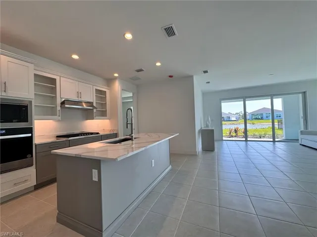 Kitchen featuring stainless steel appliances, under cabinet range hood, a sink, open floor plan, and light tile patterned floors
