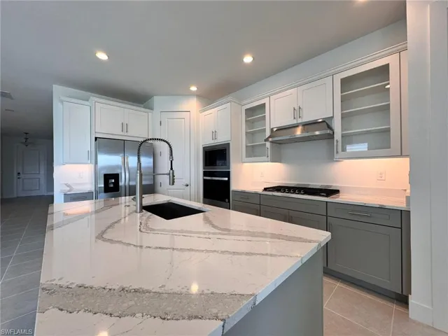 Kitchen featuring black cooktop, oven, under cabinet range hood, a sink, and stainless steel fridge with ice dispenser
