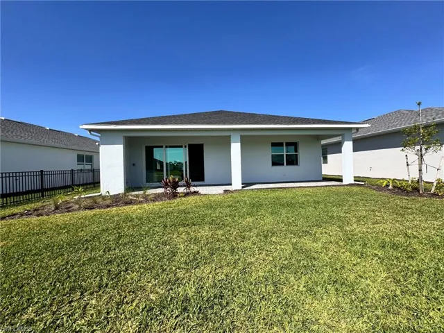 Rear view of house featuring a lawn, fence, and stucco siding