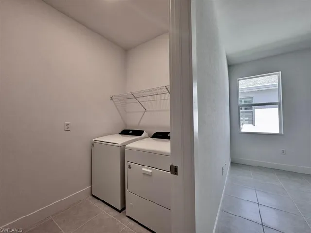 Laundry area with washer and clothes dryer, laundry area, baseboards, and light tile patterned floors