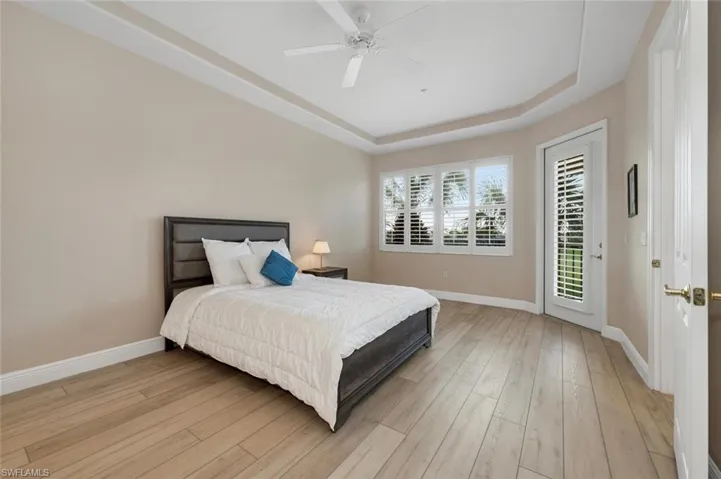 Bedroom featuring access to exterior, light wood-type flooring, a raised ceiling, and ceiling fan