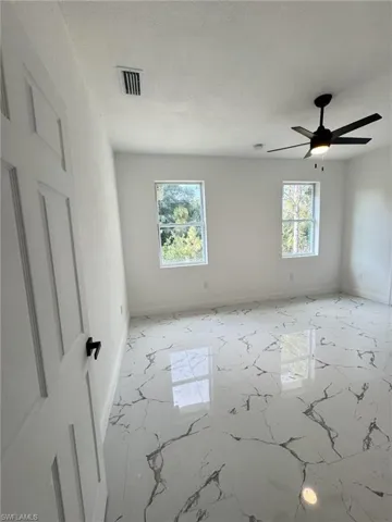 Empty room featuring baseboards, marble finish floors, and ceiling fan