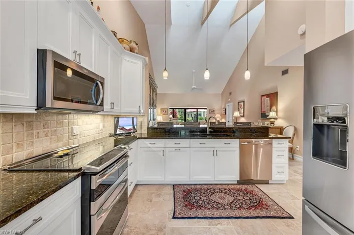 Kitchen featuring dark stone counters, appliances with stainless steel finishes, a peninsula, white cabinetry, and a sink