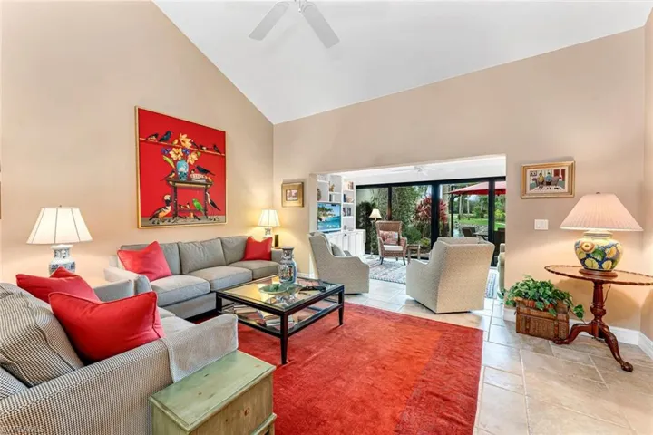 Living room with high vaulted ceiling, tile patterned floors, a ceiling fan, and baseboards