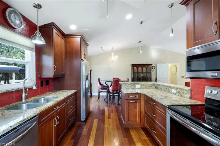Kitchen with wood-type flooring, sink, hanging light fixtures, decorative backsplash, and stainless steel appliances