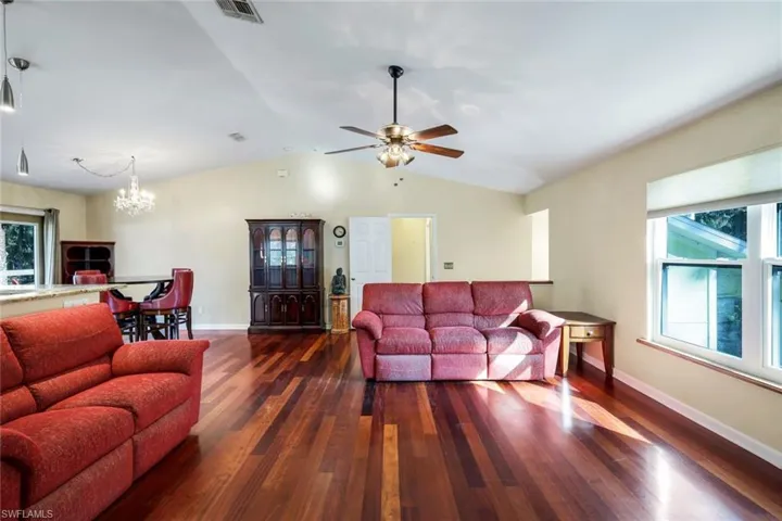 Living room with ceiling fan with notable chandelier, hardwood / wood-style flooring, and vaulted ceiling