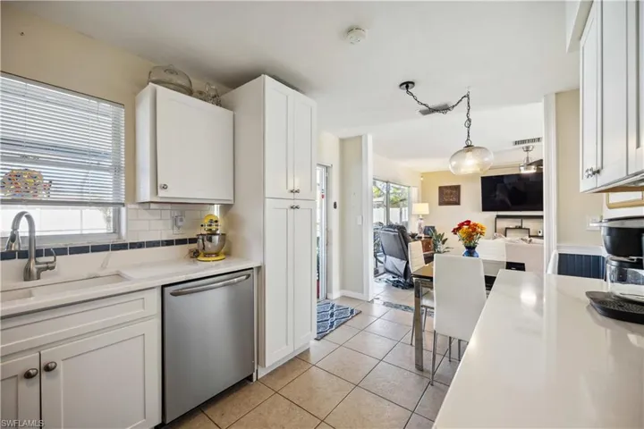 Kitchen featuring stainless steel dishwasher, a sink, light tile patterned floors, white cabinetry, and tasteful backsplash