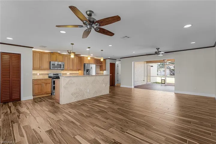 Kitchen featuring open floor plan, hanging light fixtures, ornamental molding, wood tiled floors, and stainless steel appliances