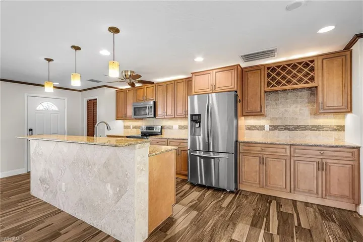 Kitchen with stainless steel appliances, light stone countertops, pendant lighting, dark wood-type flooring, and a kitchen island with sink