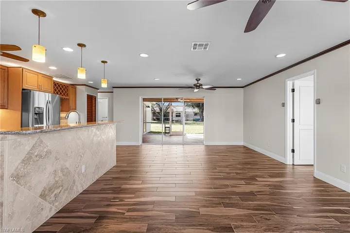 Kitchen with wood tiled floors, decorative light fixtures, crown molding, a ceiling fan, and stainless steel refrigerator with ice dispenser