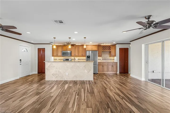 Kitchen with ceiling fan, hanging light fixtures, wood finish cabinets, dark wood-type flooring, and crown molding