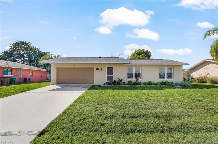 Ranch-style home with a front lawn, driveway, an attached garage, and stucco siding