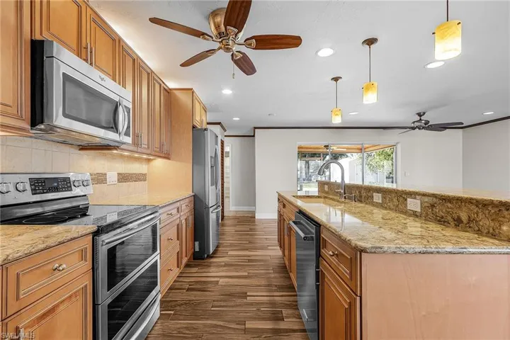 Kitchen featuring a ceiling fan, stainless steel appliances, light stone counters, dark wood-style flooring, and decorative light fixtures