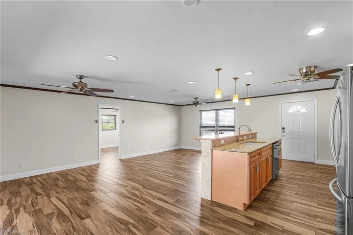 Kitchen featuring open floor plan, a ceiling fan, light stone counters, a kitchen island with sink, and stainless steel appliances