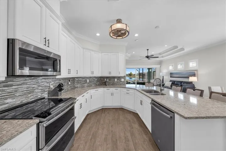 Kitchen with appliances with stainless steel finishes, light stone counters, white cabinets, recessed lighting, and ornamental molding