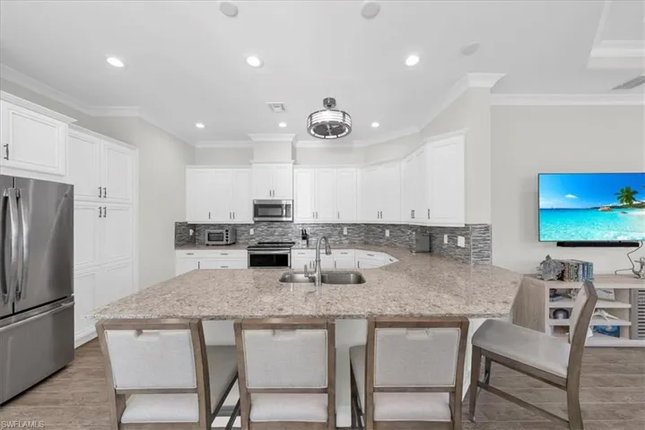 Kitchen featuring stainless steel appliances, backsplash, a breakfast bar area, ornamental molding, and white cabinets