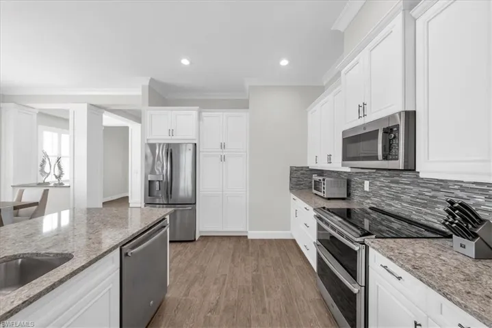 Kitchen with appliances with stainless steel finishes, crown molding, white cabinetry, light stone counters, and open floor plan