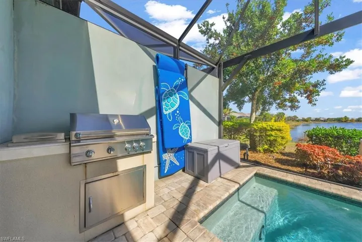 View of swimming pool featuring a lanai, exterior kitchen, a patio, a water view, and a swimming pool