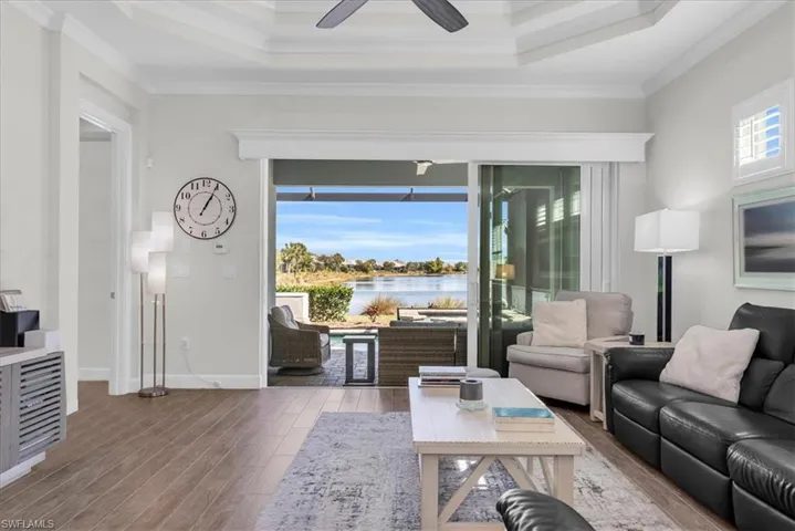 Living area featuring crown molding, wood finished floors, a tray ceiling, a water view, and a ceiling fan