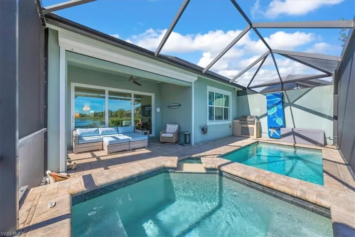 View of swimming pool with a sunroom, a patio area, glass enclosure, a pool with connected hot tub, and a grill