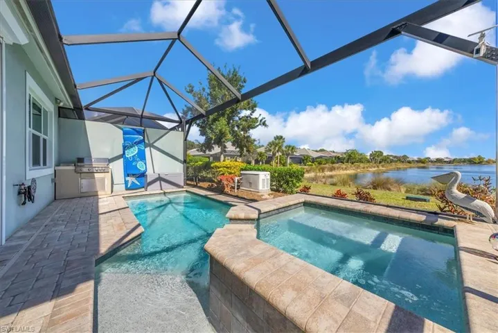 View of pool featuring a patio area, a sunroom, glass enclosure, an outdoor kitchen, and a pool with connected hot tub