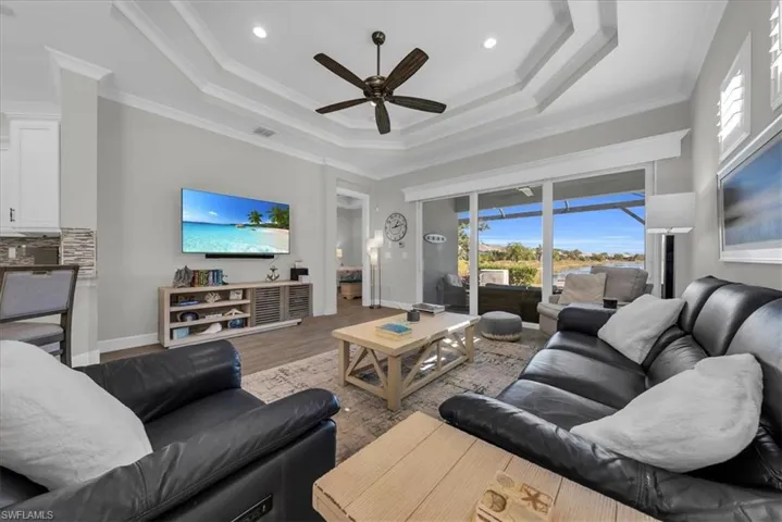 Living room with ornamental molding, wood finished floors, a ceiling fan, a raised ceiling, and recessed lighting