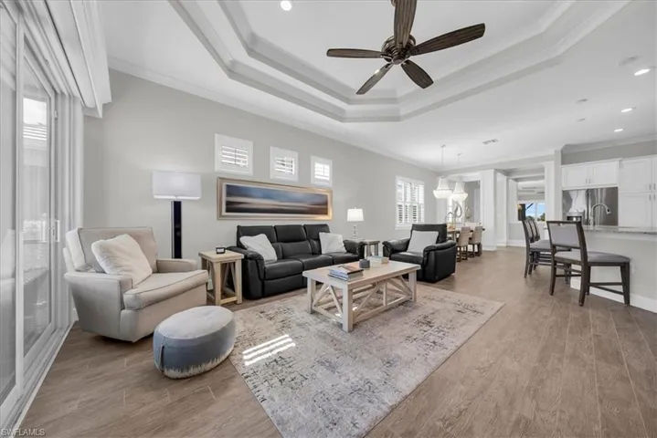 Living room with light wood-style floors, ornamental molding, ceiling fan, a tray ceiling, and recessed lighting