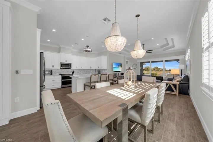 Dining area featuring ornamental molding, a chandelier, dark wood-style flooring, a raised ceiling, and ceiling fan