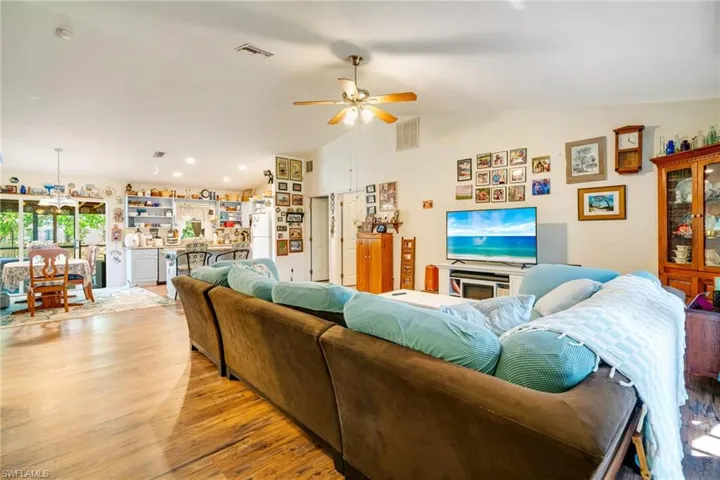 Living area featuring light wood finished floors, visible vents, lofted ceiling, and a ceiling fan